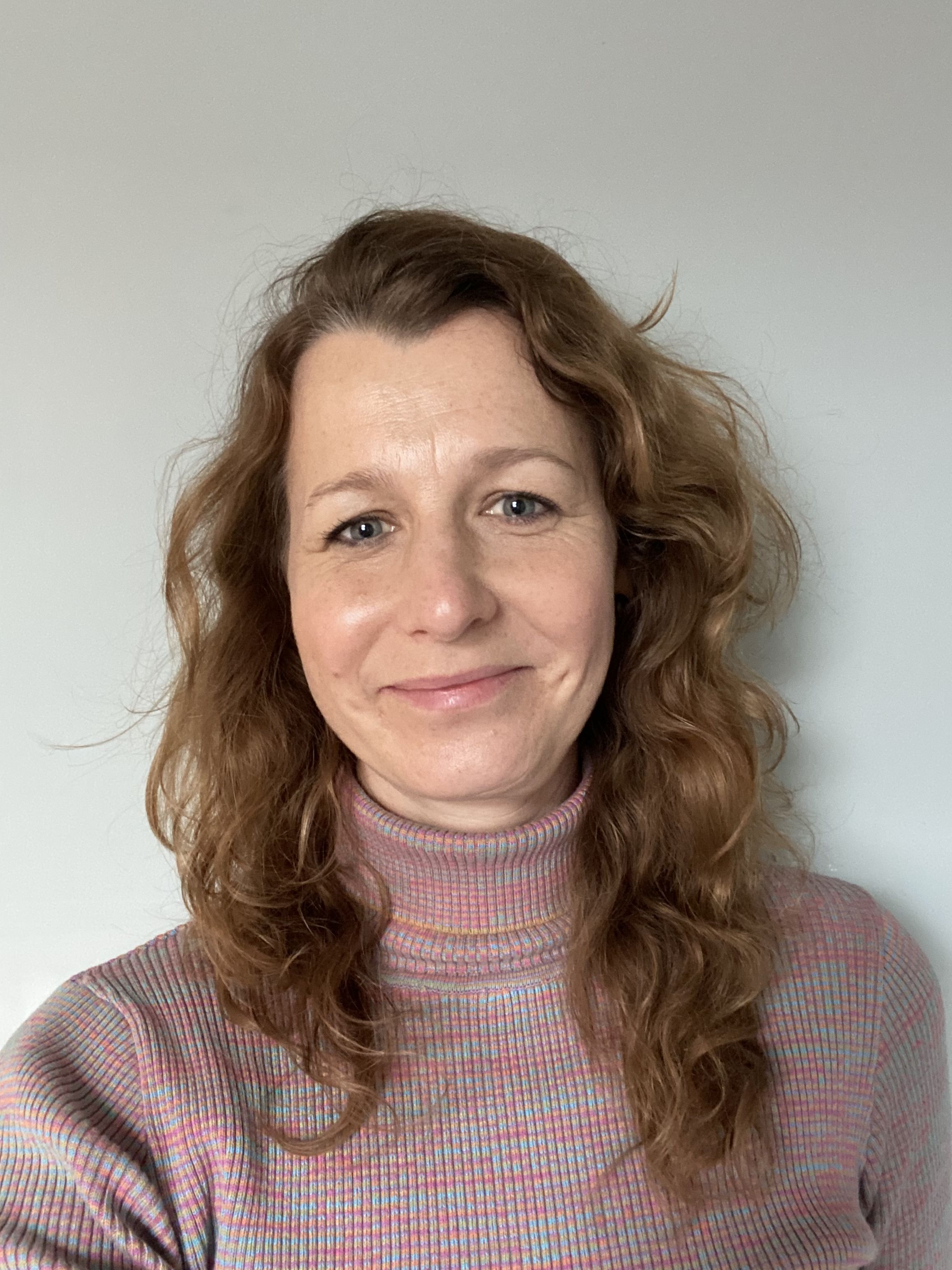 Martha Crean is standing in front of a light-coloured wall, smiling directly at the camera.