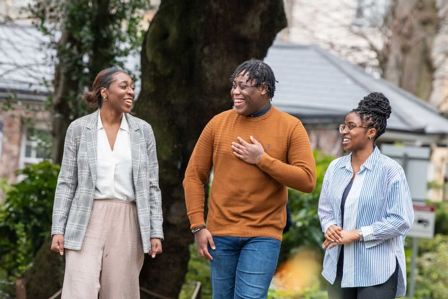 Three students walk through Royal Fort Gardens and laugh.