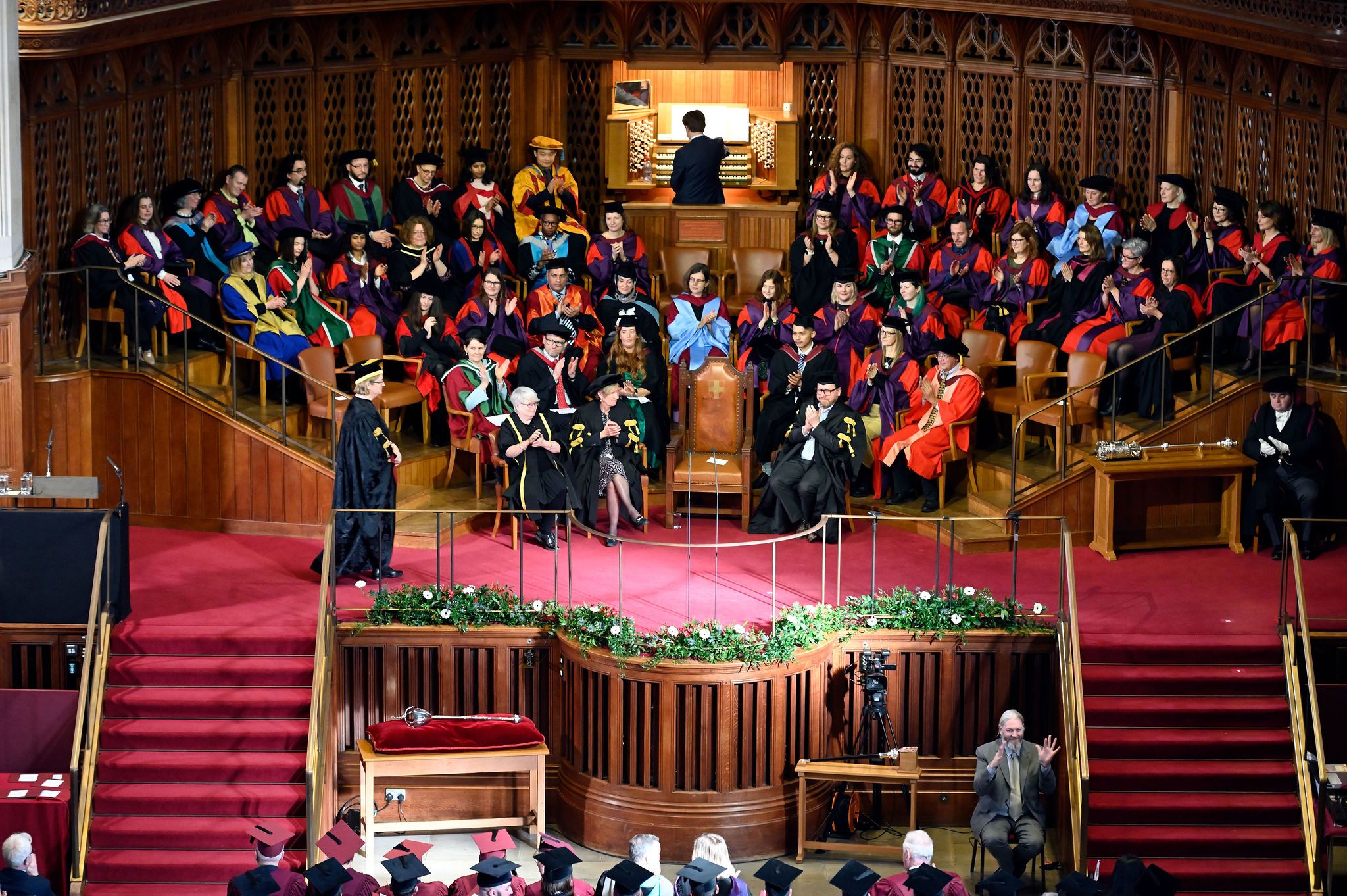 The presiding officer and staff their academic robes on the stage in the Great Hall of Wills Memorial Building.
