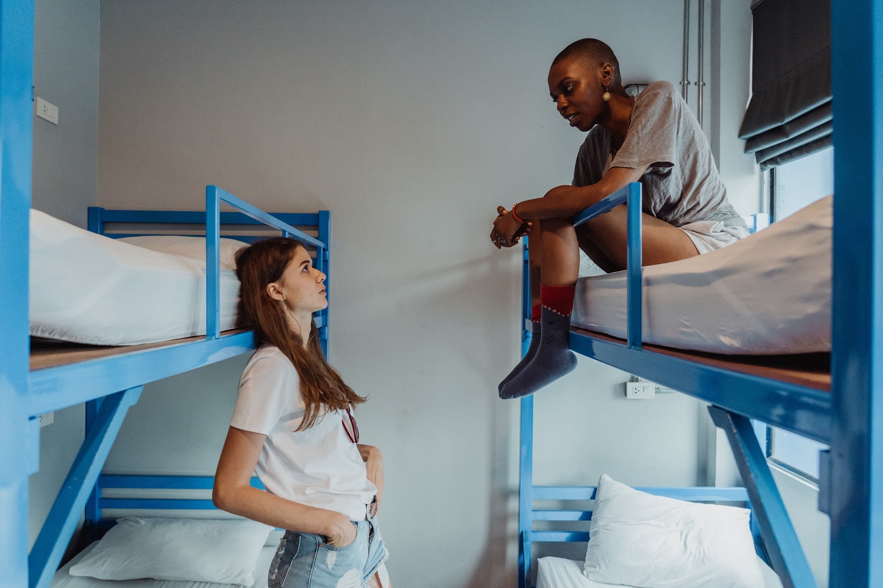 One black woman and one white woman talking seriously from different bunk beds in uncomfortable accommodation