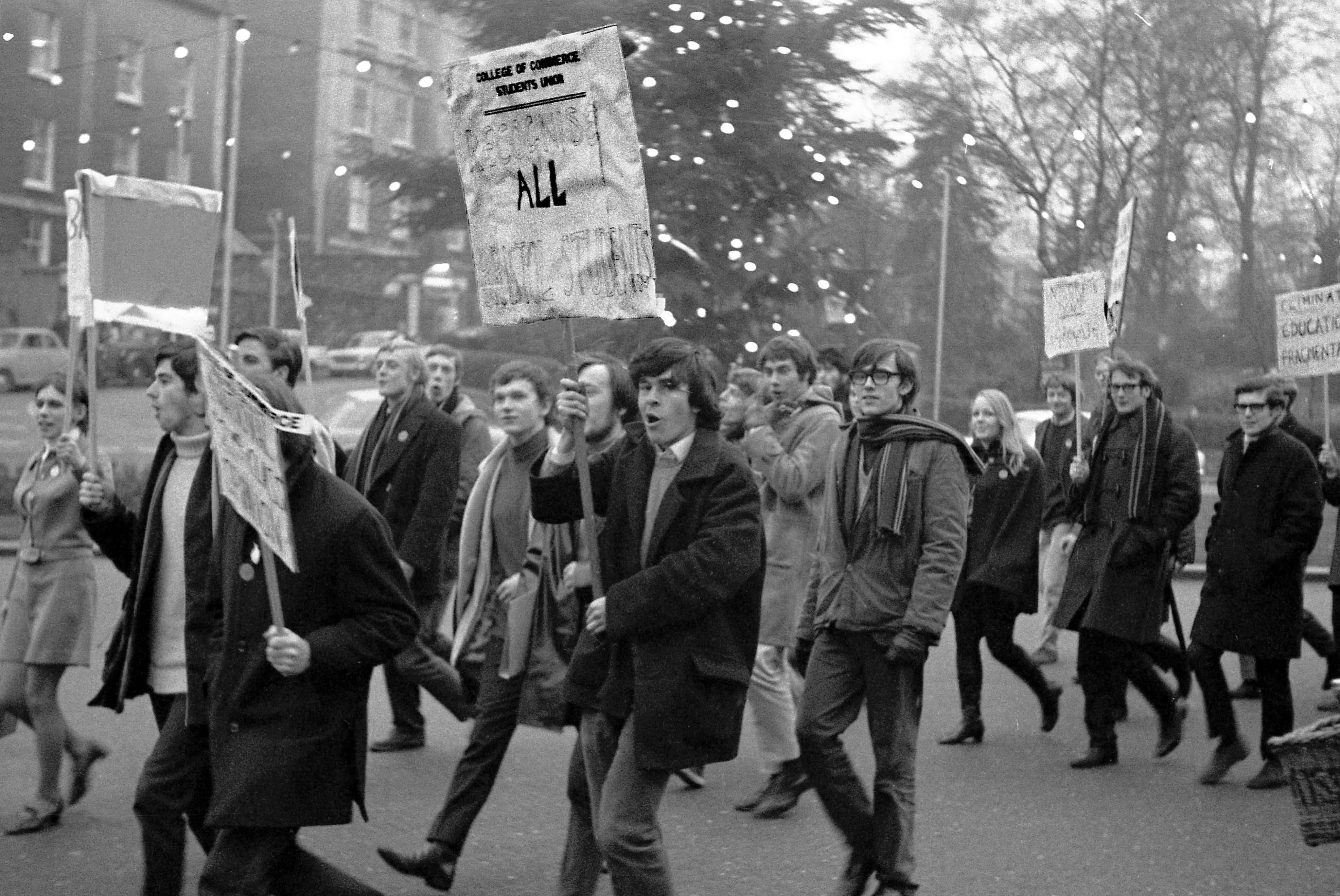 A group of around 20 students, some holding placards, walking together in protest. They are dressed in warm winter clothing.