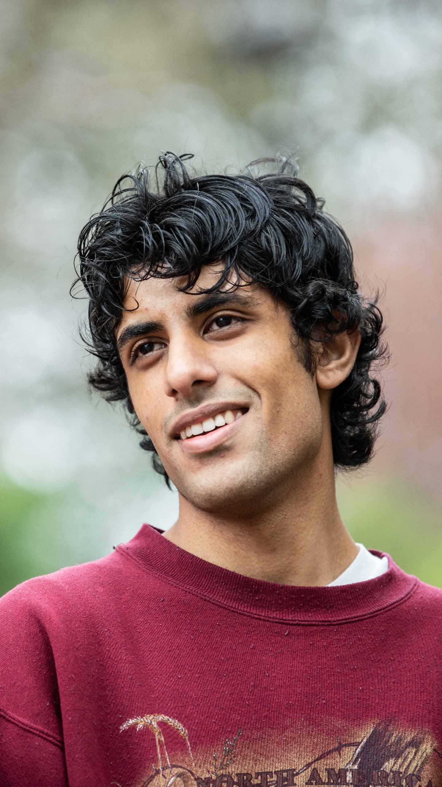 Raphael is smiling as he looks away into the distance to the left of the camera. He is wearing a maroon-coloured jumper.