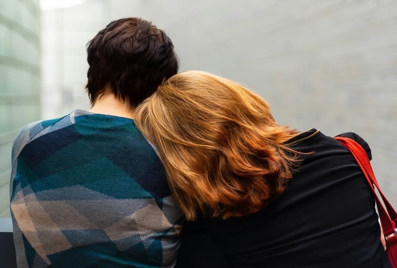 Couple sitting together with one person's head leaning on others shoulder.