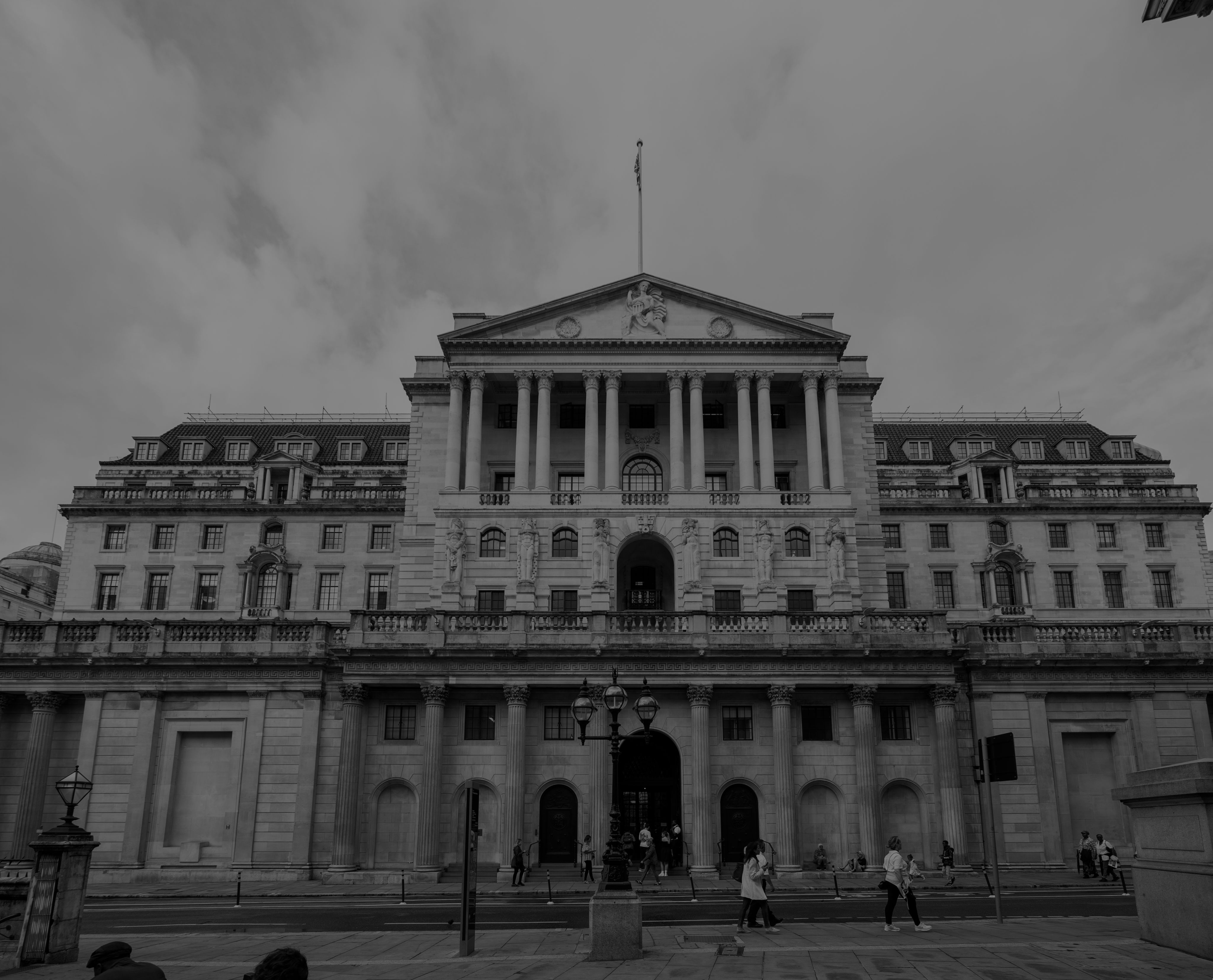 The facade of the historic Bank of England building in black and white with a gloomy sky in the background